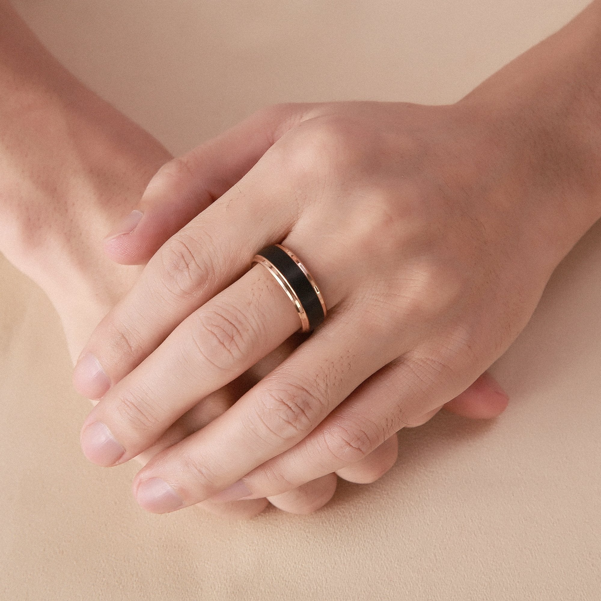 Close-up of a hand wearing a black ring on a beige background